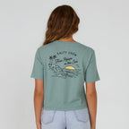 Girl wearing a sage Salty Crew Lookout Women's Crop T-Shirt with sunset scene